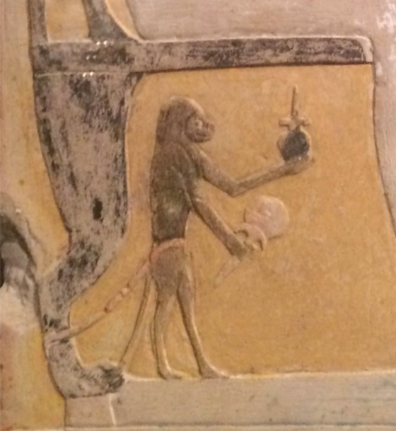<em>Detail of a simian beneath the chair of its owners on a stele in Baltimore, Walters Art Museum 22.92 holding a mirror with a floral formed handle.</em>